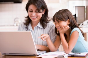 photo of Woman and young girl in kitchen with laptop and paperwork smiling