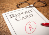 MCPS High School Rankings Based on Maryland School Report Card Scores Report card on an oak desk with a red “A” written on it . A red pen in the foreground and glasses in the background.